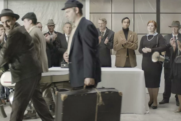 Menschen mit Koffern in einer Bahnhofshalle im Stil der 60er Jahre